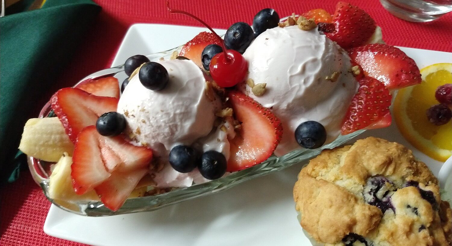 Oval glass dish filled with ice cream and fruit with a fruit muffin on the side