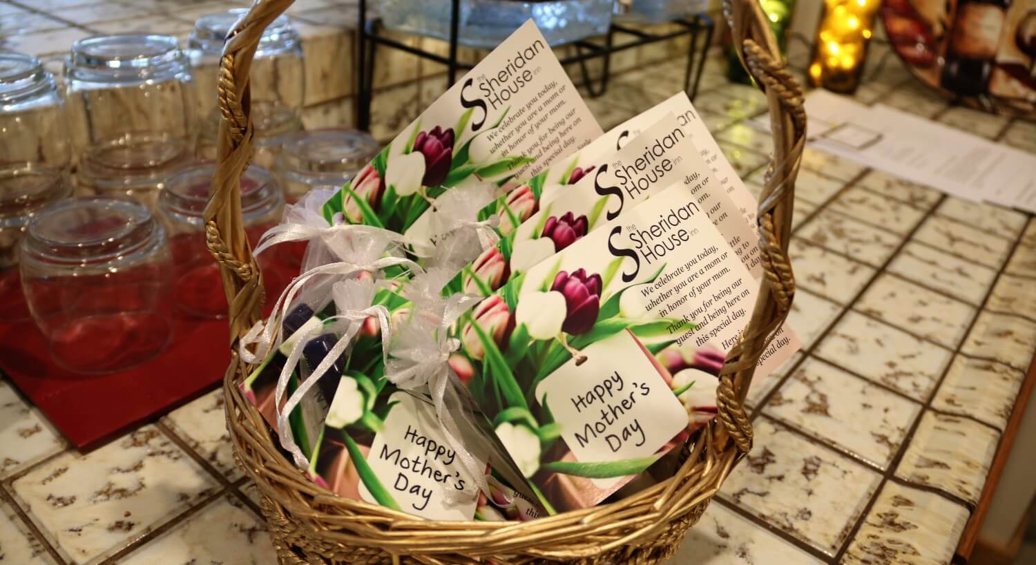 Basket with tall handle filled with white gift bags and flowered cards for Mother's Day