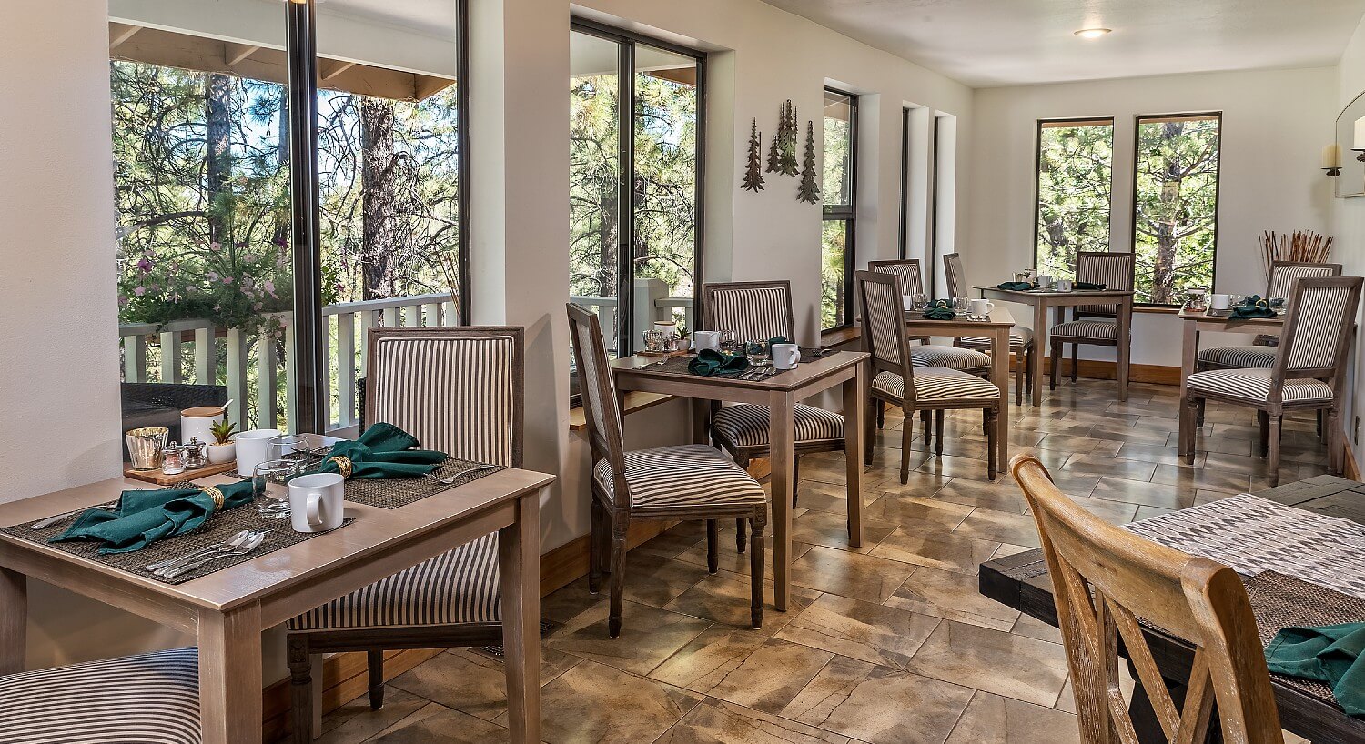 Large dining room surrounded by tall windows and six breakfast tables each set for two