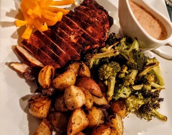 plate with pile of browned potato pieces, broccoli, chicken with a coating, gravy boat and a pepper