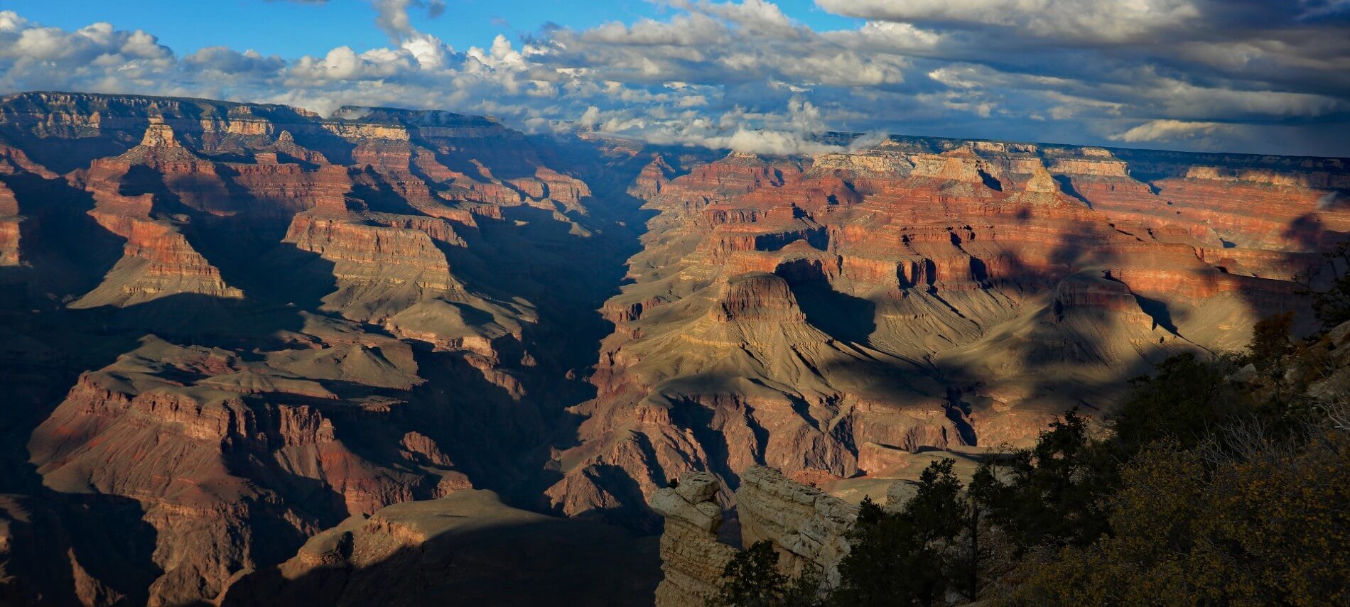 Grand Canyon view at sunset - rocks turning red and yellow with large shadows and blue sky