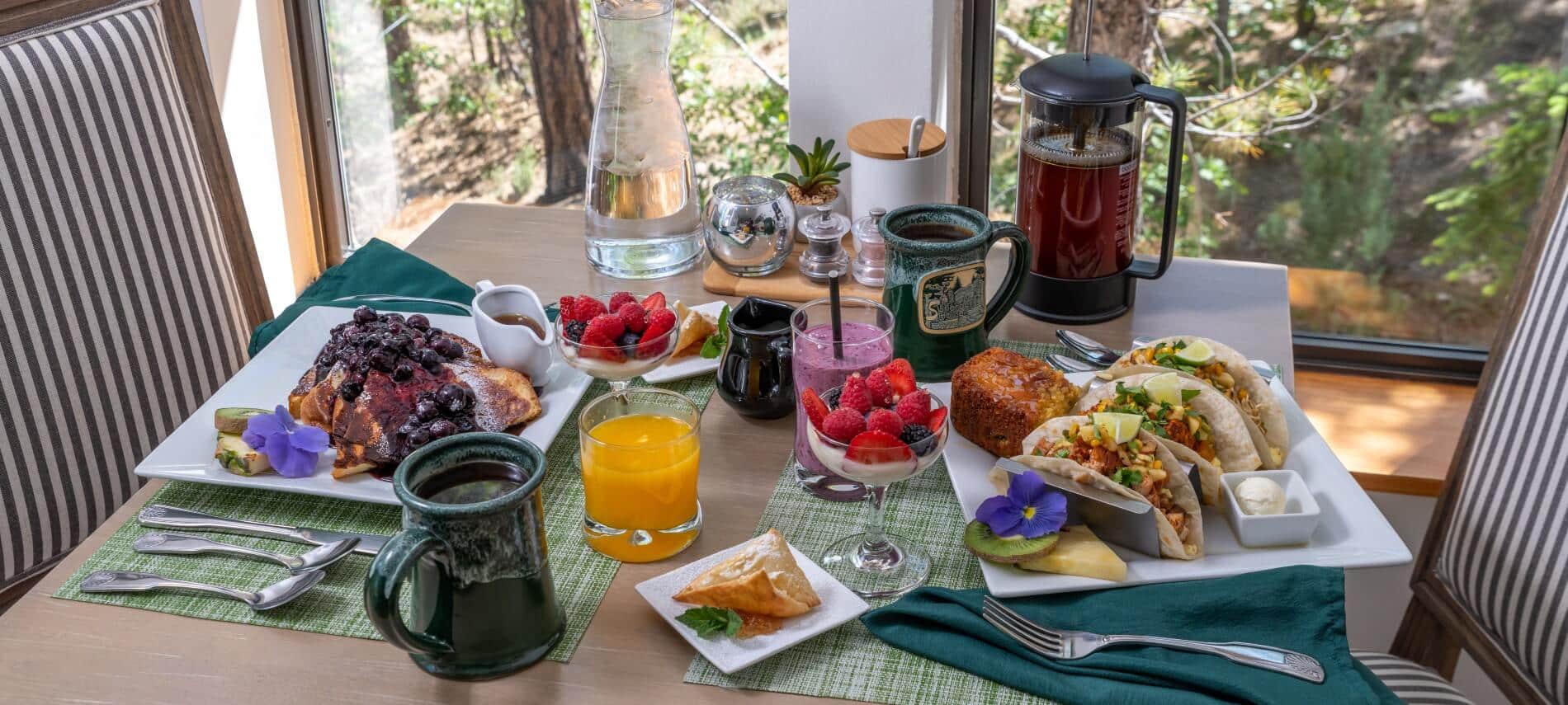 Black wicker table on an outside patio set for for two with plates of breakfast, coffee, juice and glass dishes of fruit