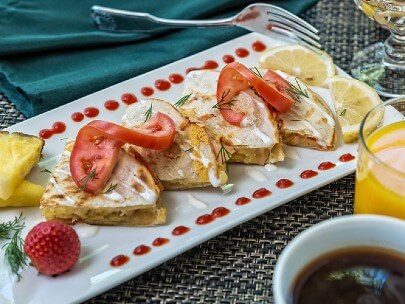 Rectangular white plate with breakfast quesadilla, sliced tomatoes and fruit and coffee and orange juice on the side