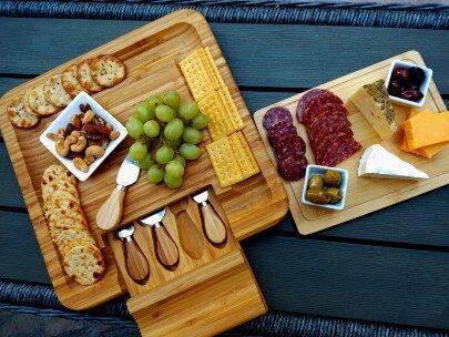 Two wooden charcuterie boards with fruit, crackers, cheese, meat and nuts on a black table