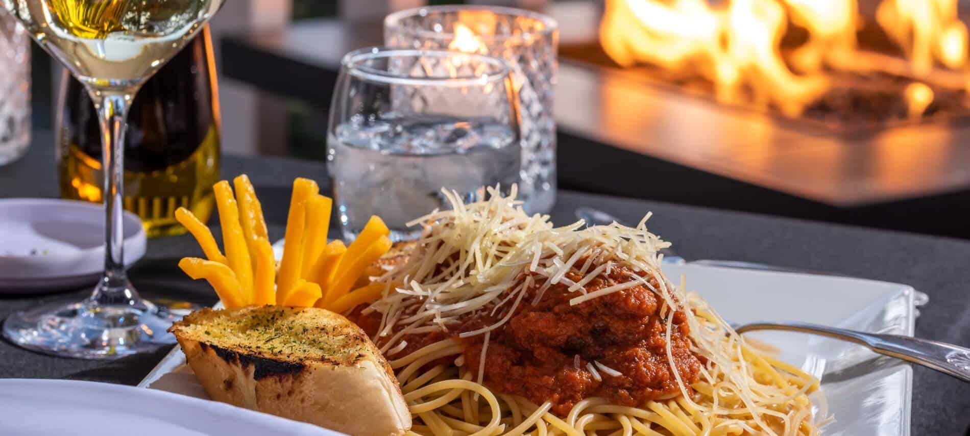 white plate with a mound of spaghetti sauce covering matballs on top of spaghetti noodles with garlic bread and a pepper cut like a flower