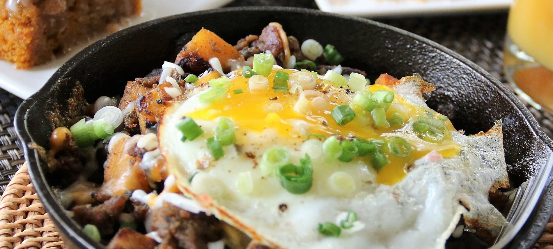 Cast iron pan filled with breakfast hash of meat and potatoes topped with fried eggs and diced green onion