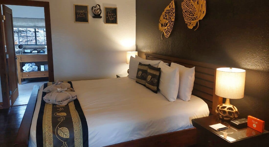 dark wooden bed with lamps on both sides under a black wall with gold aspen leaves decor and bathroom in the background