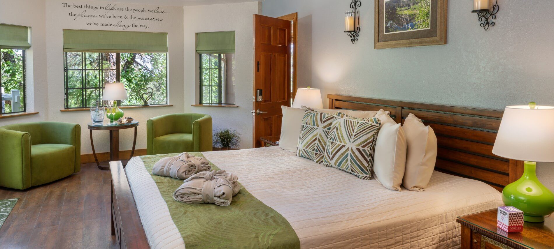 bed room with king bed with cream colored blanket, with green swivel chairs and a table in front of a large window