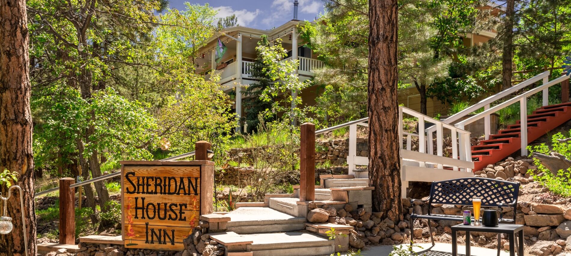 Large wooden sign with inn name at the base of a tall staircase leading up to a home with large outdoor deck