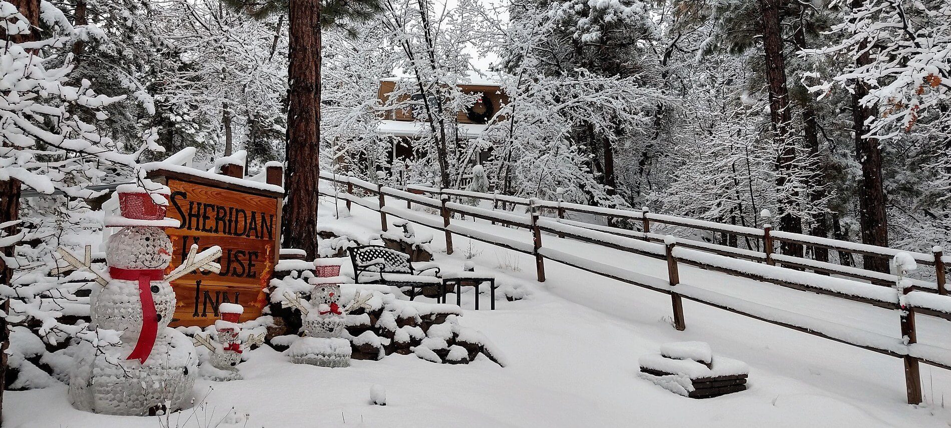 Driveway up to a home flanked by a wooden fence, with inn sign and snowman amidst freshly fallen snow