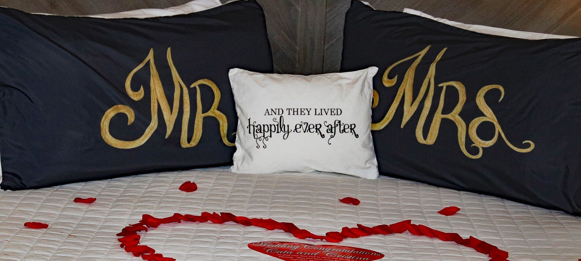 Bed with Mr and Mrs pillows and red flower petals in the shape of a heart