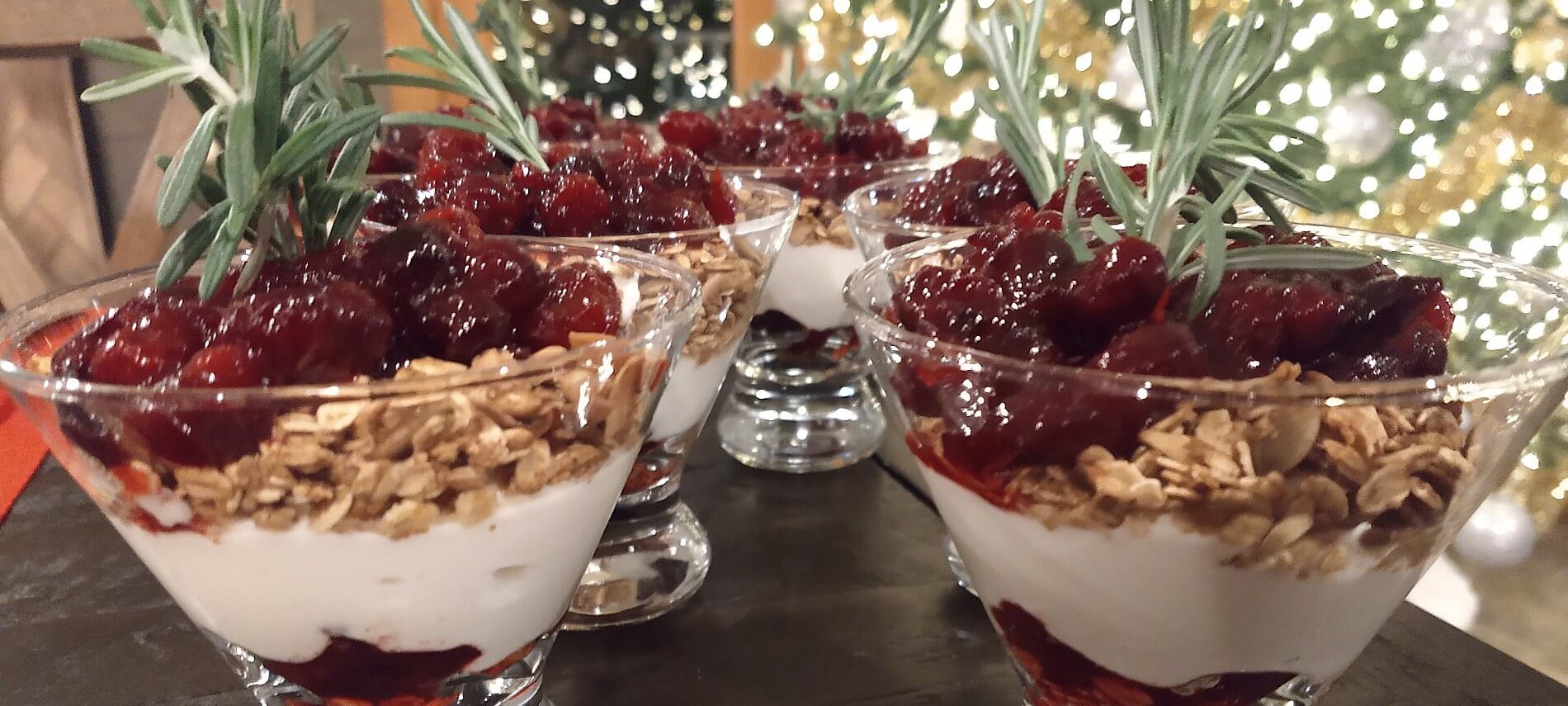 Five glass dishes filled with white yogurt, granola and red cherries on a black table
