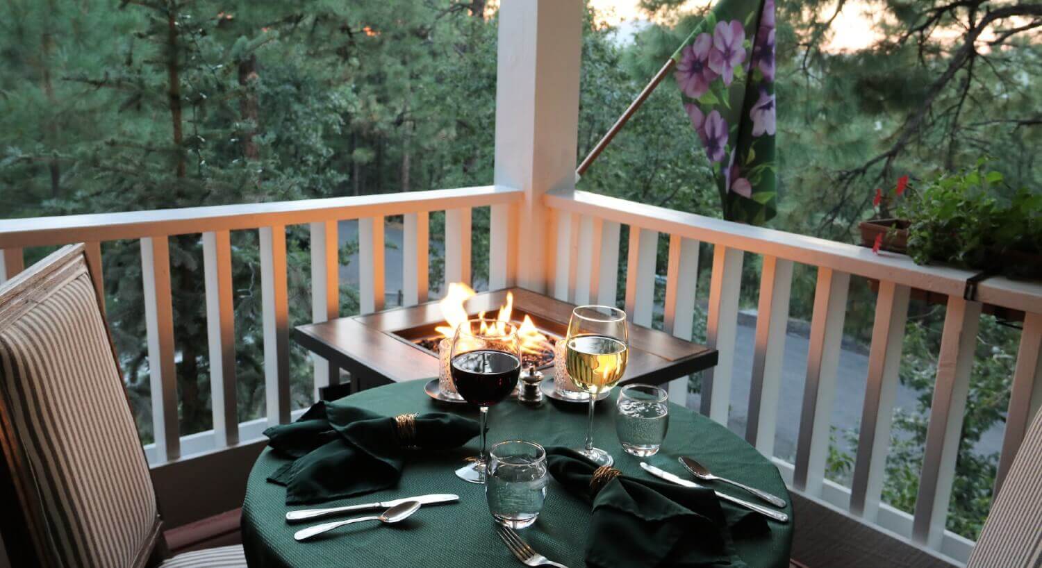 balcony table set with green linens and wine glasses, striped upholstered chairs with fire pit burning in the corner
