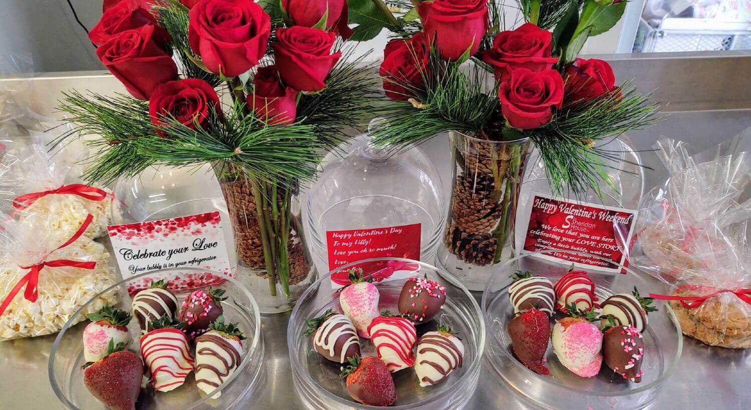 clear vases with red roses with greenery and candy dishes with chocolate covered strawberries on table plus popcorn in bags