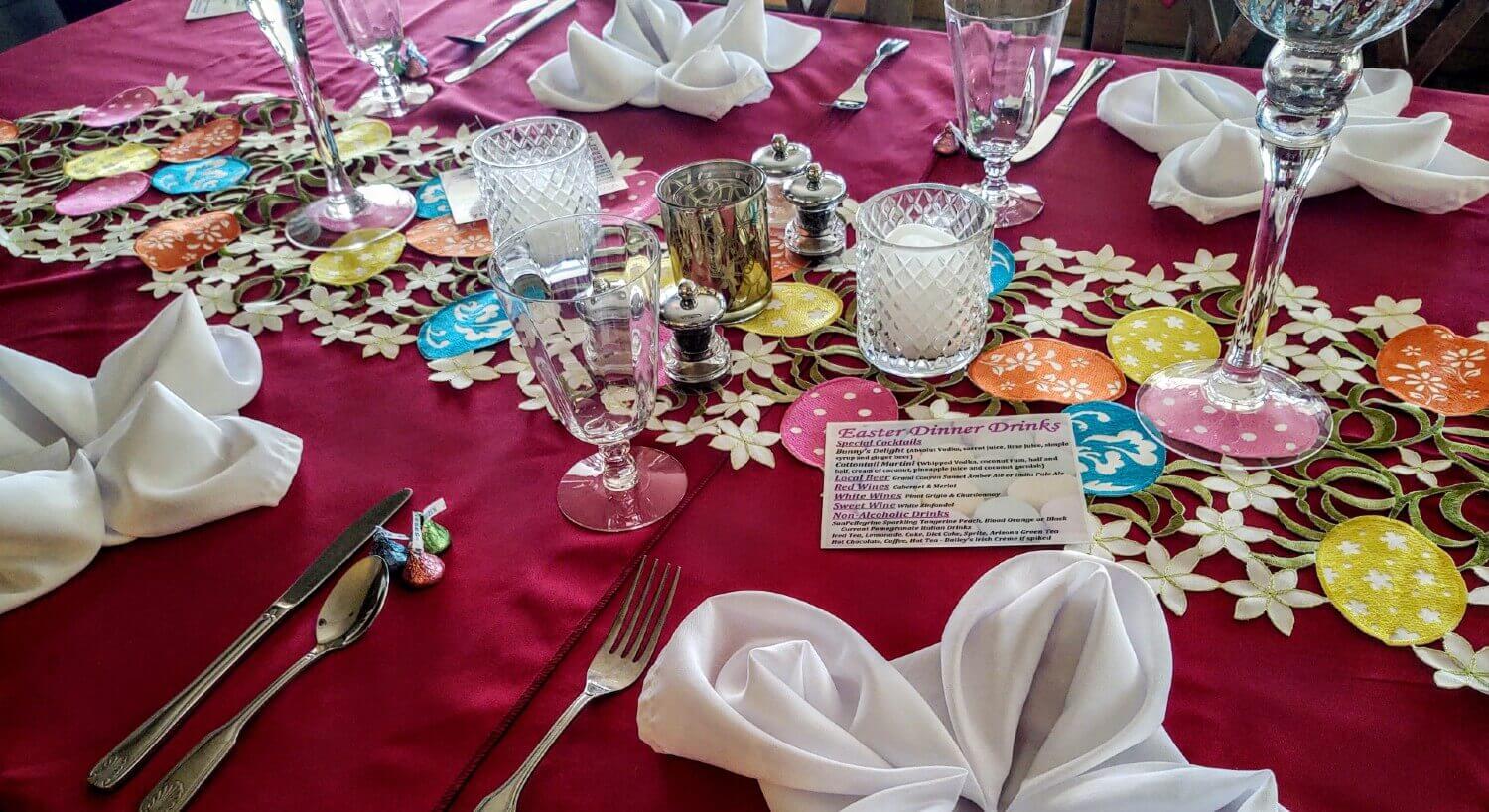 table with burgundy cloth and white linen napkins, table runner with felt easter eggs and recipe card for Easter dinner drinks