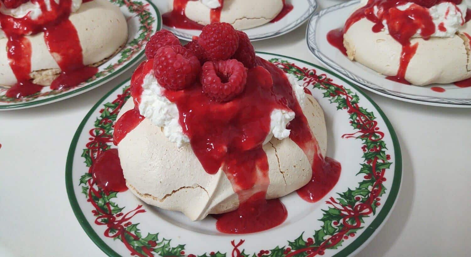 small Christmas plates with a white meringue tart covered with whipped cream, red sauce and raspberries