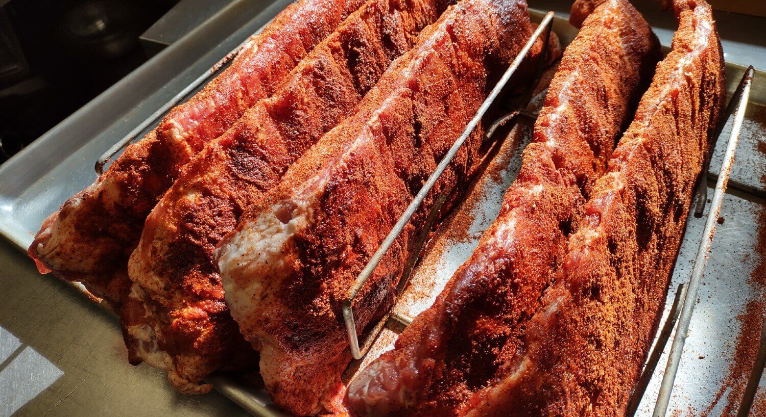 full racks of ribs garnished with seasoning sitting on metal trays