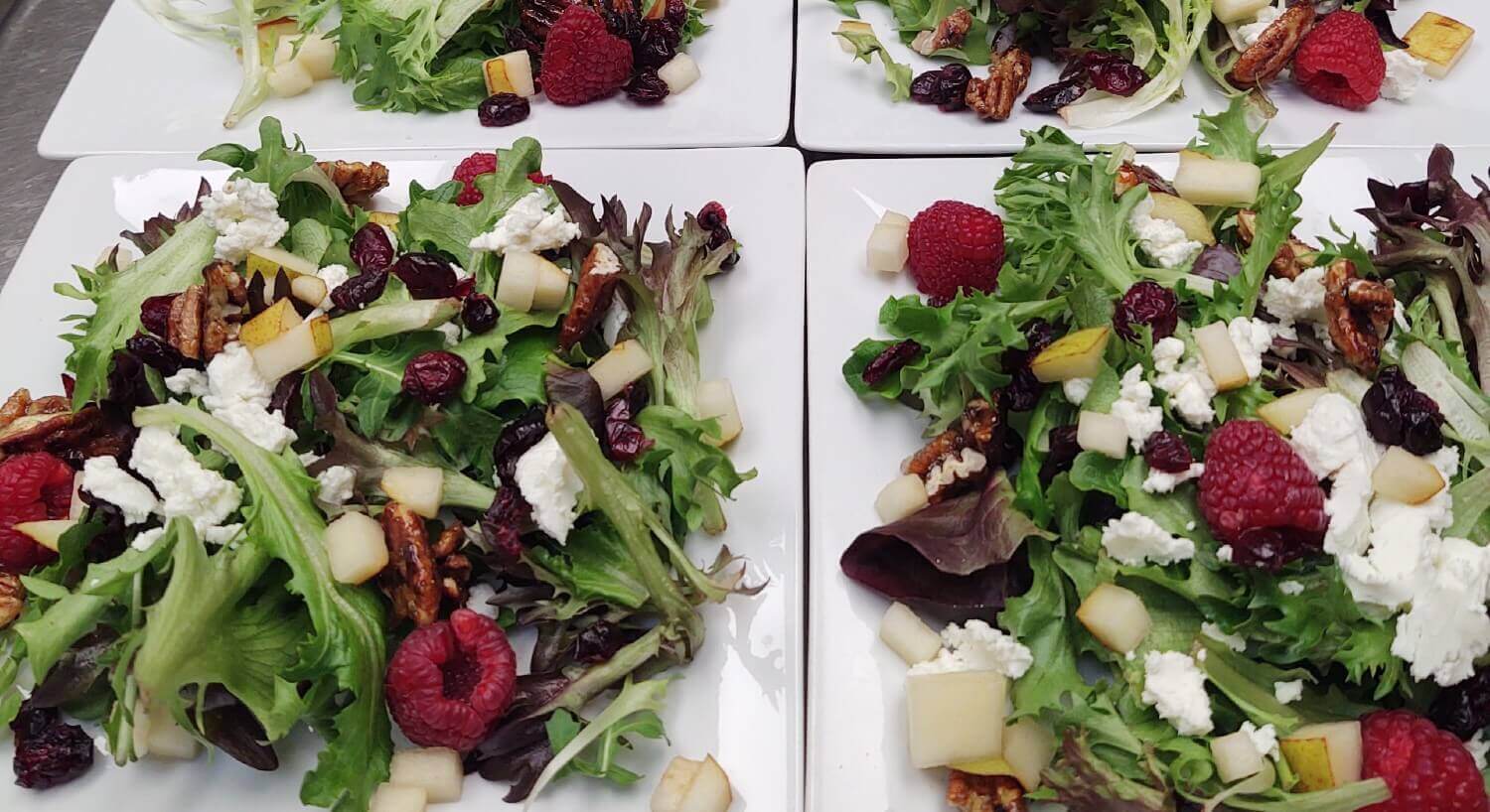 white square plates with salads including raspberries, cheese and nuts ready to be served