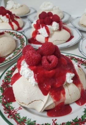 small Christmas plates with a white meringue tart covered with whipped cream, red sauce and raspberries