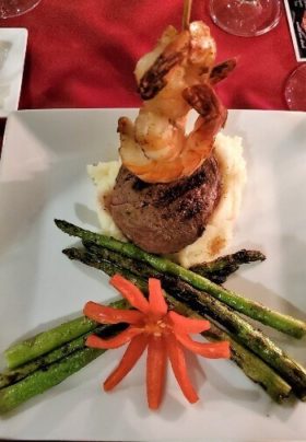 white plate with asparagus, an orange pepper flower, mashed potatoes, beef and shrimp on a bamboo skewer