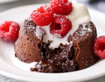 chocolate cake oozing with chocolate filling, with whipped cream on top and fresh raspberries