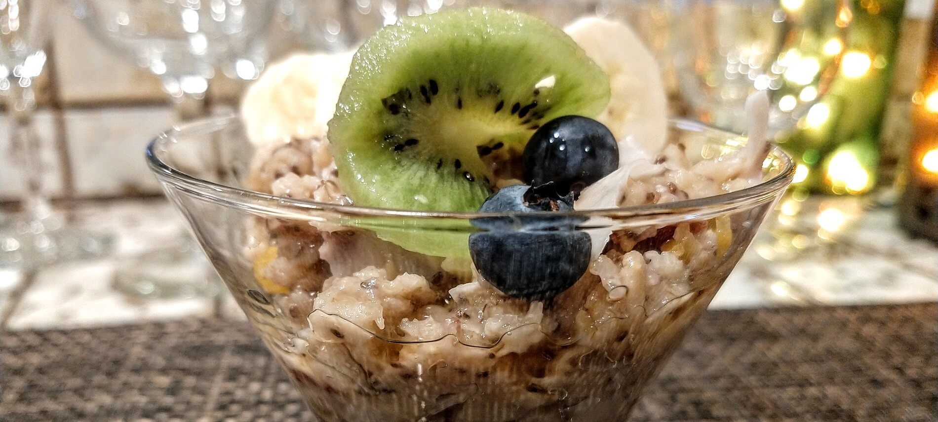 Glass bowl with homemade oatmeal and slice of kiwi, blueberries and sliced bananas