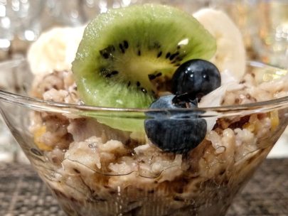 Glass bowl with homemade oatmeal and slice of kiwi, blueberries and sliced bananas