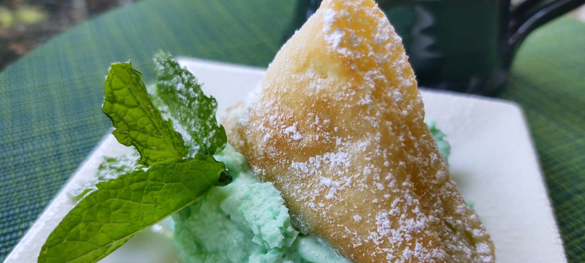 triangular puff pastry on top of a green whipped cream with a mint leaf