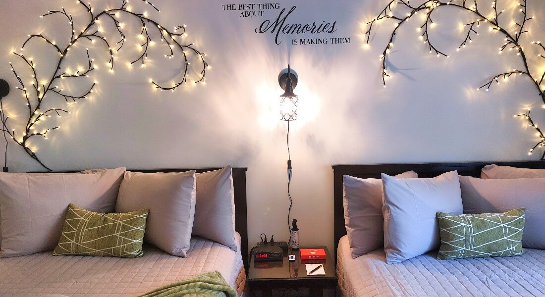 part of 2 beds with lots of pillows against a wall with a quote "the best part of Memories is making them" and lighted willow branches