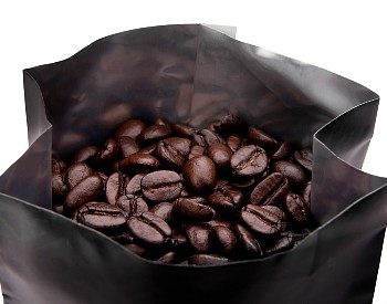 Open bag of dark brown coffee beans against a white background