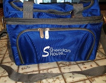 Blue cooler with grey straps and zippered pockets sitting on a tiled countertop