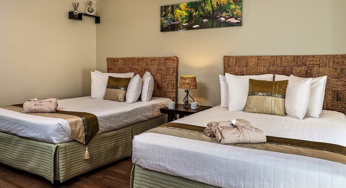 Two double beds with wicker headboards and white comforters in a room with art work on cream walls