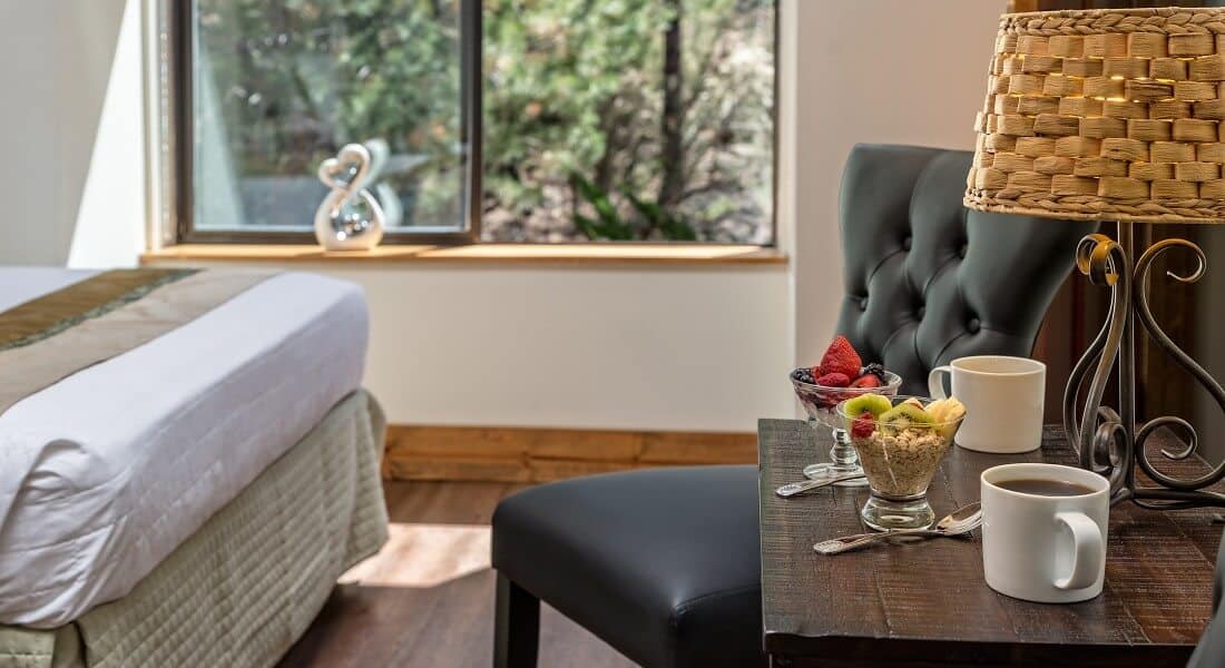 Guest room with large bright window and wooden table holding coffee cups and glass bowls of oatmeal and fruit