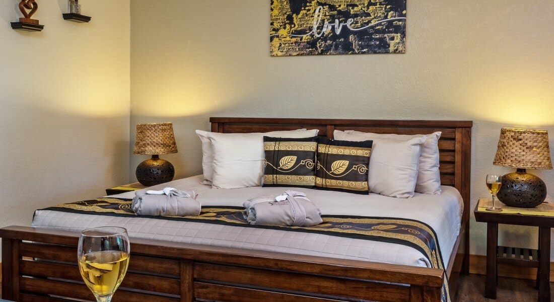 Wooden king bed with white and black bedding, two night tables and art work on cream walls