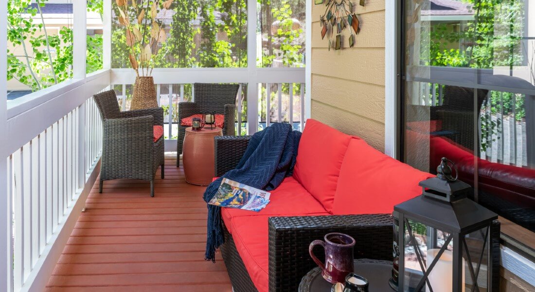 Two black wicker club chairs and a table with wine and plate of snacks in the corner of a porch patio with white railings