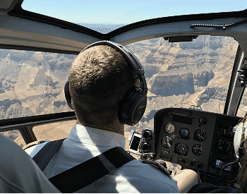 Man in white shirt and headphones piloting a helicopter with views of rock and canyon through the windows