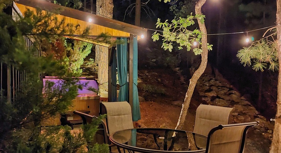 outdoor patio at night with lights, a glass table with chairs and an open lighted hot tub