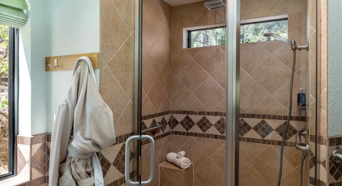 Large walk-in tiled rainshower with open glass door and bathroom on a hook