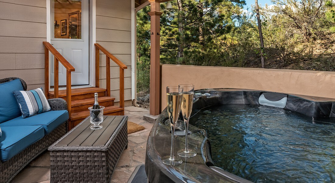 Patio with wicker love seat with blue cushions, table and hot tub with two glasses of champagne
