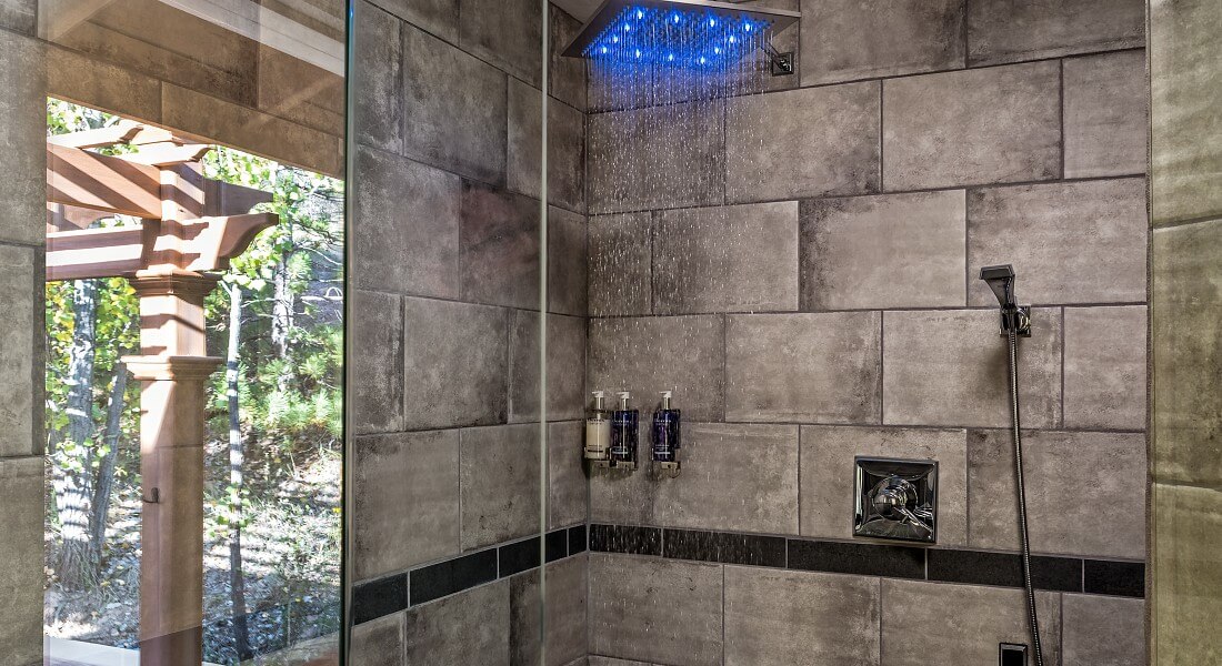 Gorgeous stand up shower with large window, grey tile, glass doors and rainfall showerhead lit with blue lights