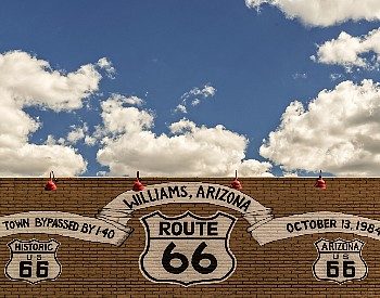 Side of a brown brick building with white painted signs and blue sky with clouds above