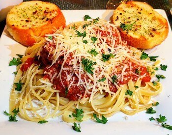 plate of spaghetti noodles with red sauce, meatballs, parmesan cheese and 2 pieces of garlic covered French bread