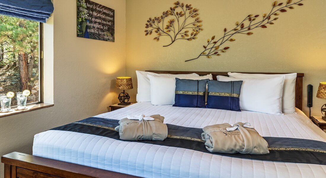 Wood framed king sized bed with white comforter and blue pillows in a room with bright window art work on cream walls