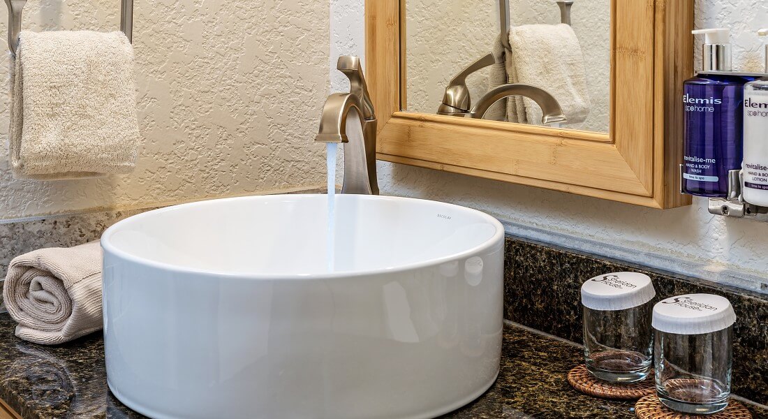 Modern white sink with silver faucet on granite countertop below mirror with light wood frame