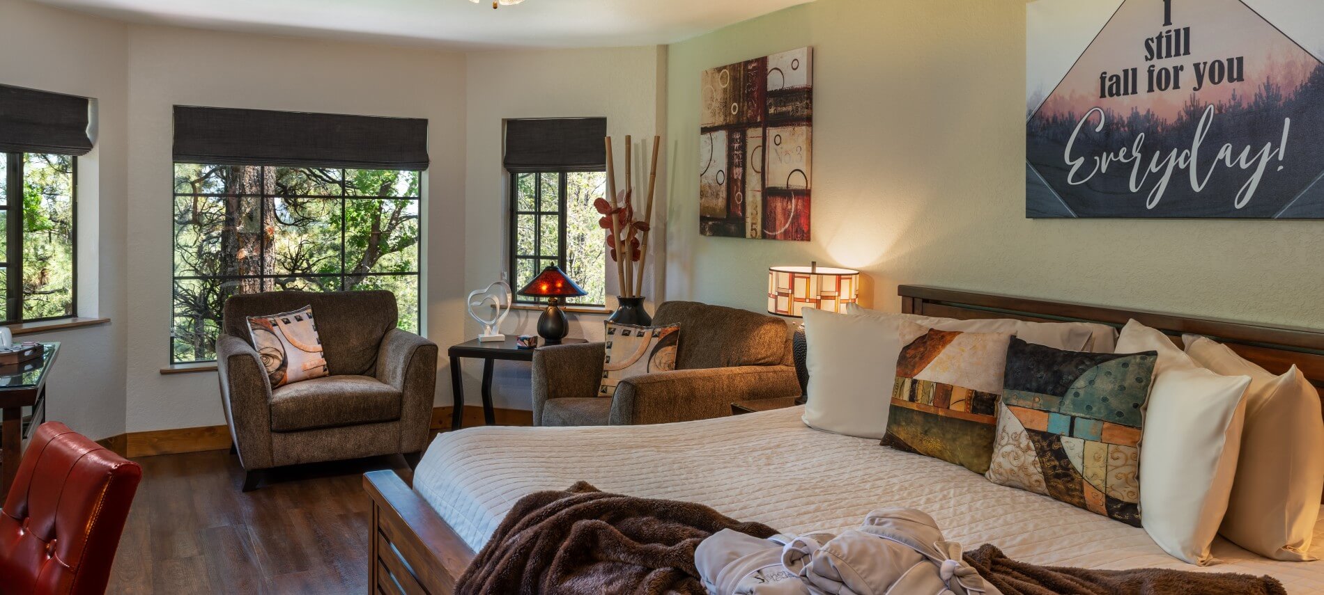 King bed with white comforter and green accents in a room with large windows and sitting area with two wicker chairs