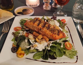 plate with lettuce, vegetables with a salmon on top ablesilverware and tablecloth and drinks