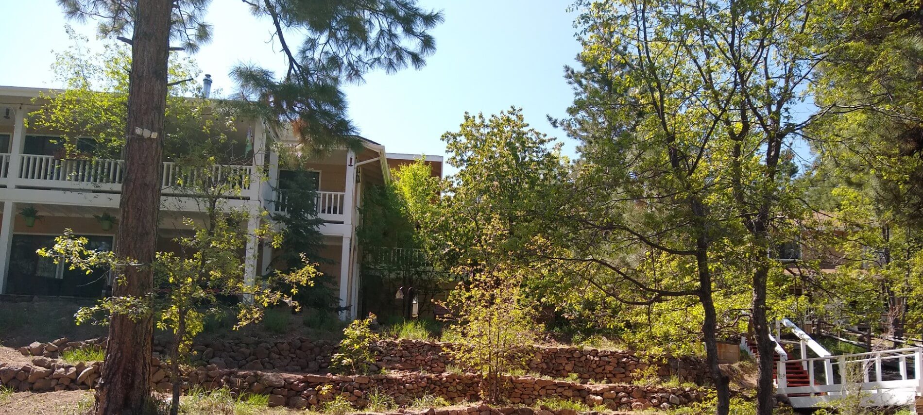 Mutli-level house with balconies surround by woods, wooden bridge, rock wall