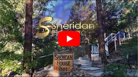 Sign of Sheridan House Inn beside a walkway with large pine trees.