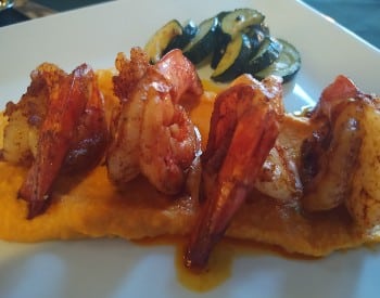Plate with 4 butterflied cooked shrimp on orange mashed sweet potatoes and sauteed zucchini