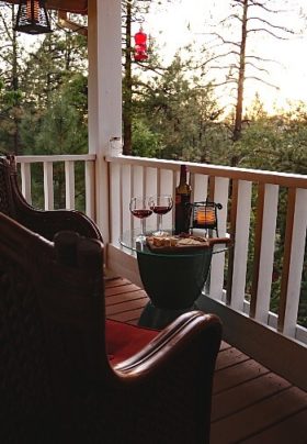 Two brown chairs with a glass-topped side table holding a wine bottle, glasses and plate of snacks on a small outdoor patio